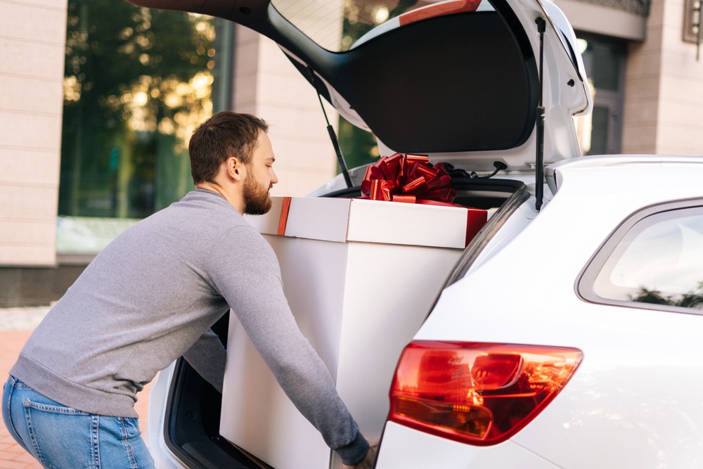 Delivery man takes a large festive box out of car.